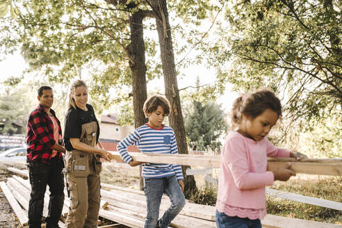 Eltern und Kinder tragen ein Holzbrett im Hinterhof - MASF21139