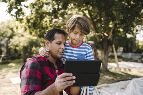 Father using digital tablet by son in yard - MASF21155