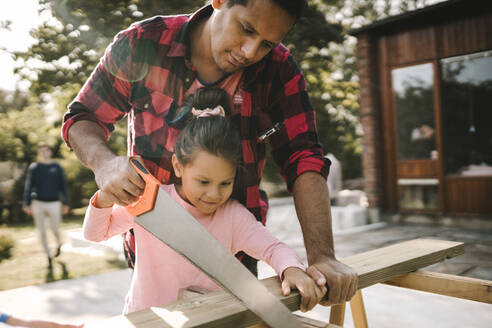 Lächelndes Mädchen beim Holzhacken mit Vater vor dem Haus - MASF21159
