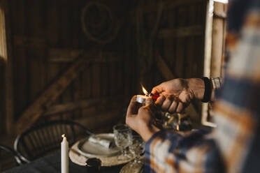 Cropped image of woman igniting candle by dining table during social gathering - MASF21213