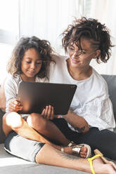 Mutter und Tochter sitzen zusammen auf dem Sofa mit digitalem Tablet - JAQF00114