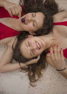 Teenage girl eating cherry while lying with sister on floor - AXHF00004