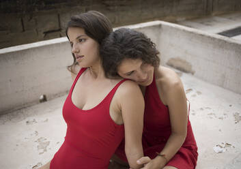 Nachdenkliche Schwestern in roter Kleidung sitzen auf der Terrasse - AXHF00006