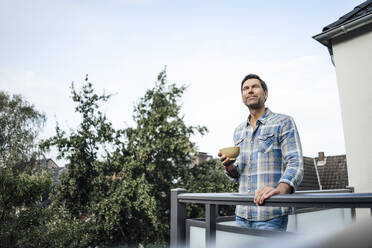 Älterer Mann träumt, während er eine Schüssel auf dem Balkon eines Hauses hält - JOSEF02690