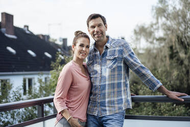 Happy mature couple in balcony standing against sky - JOSEF02709