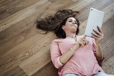 Mature woman using digital tablet while lying on floor in apartment - JOSEF02720
