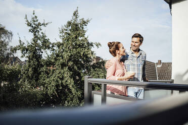 Mature couple looking at each other and smiling while standing in balcony on sunny day - JOSEF02721