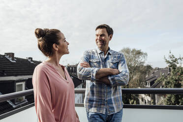 Mature man with arms crossed smiling while looking at woman in balcony - JOSEF02729