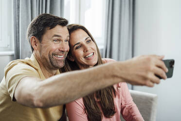 Glückliches reifes Paar spricht Selfie durch Handy zu Hause - JOSEF02738