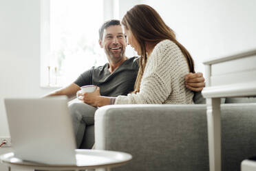 Cheerful mature couple laughing while sitting on sofa at home - JOSEF02746