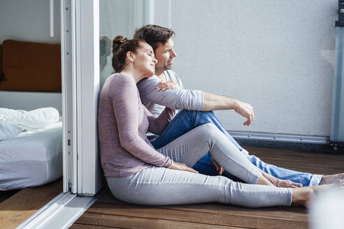 Mature couple sitting in balcony while leaning on glass during sunny day - JOSEF02767