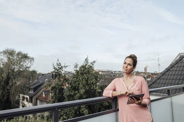 Reife Frau, die wegschaut, während sie sich auf dem Geländer eines Balkons gegen den Himmel lehnt - JOSEF02777