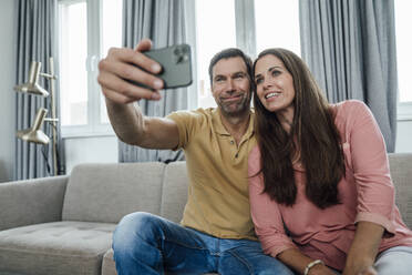 Smiling mature couple taking selfie in apartment - JOSEF02798