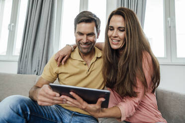 Smiling mature couple using digital tablet on sofa at home - JOSEF02803