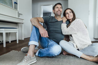 Smiling mature couple day dreaming while sitting on floor at home - JOSEF02816