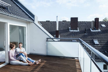 Happy couple looking at each other while sitting in balcony - JOSEF02833