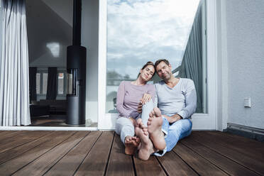 Mature couple with eyes closed sitting against glass french doors in balcony - JOSEF02834