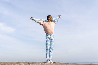 Smiling man standing with arms outstretched against sky - AFVF08004