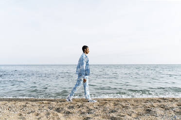 Junger Mann in Jeans-Outfit läuft gegen das Meer - AFVF08030