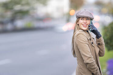 Lächelnde attraktive Frau, die auf der Straße steht und mit einem Smartphone spricht - GGGF00704