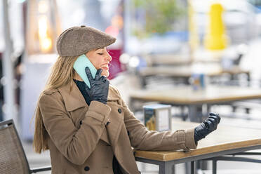 Lächelnde Frau, die in einem Straßencafé mit ihrem Smartphone telefoniert - GGGF00710