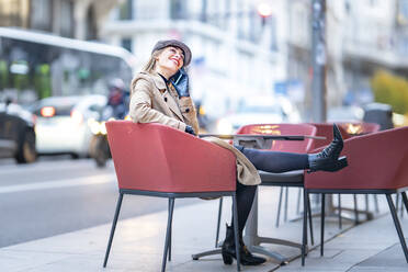 Frau, die in einem Café auf einem Stuhl sitzend mit einem Mobiltelefon spricht - GGGF00723