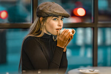 Schöne Frau trinkt Kaffee, während sie nachts in einem Cafe sitzt - GGGF00726