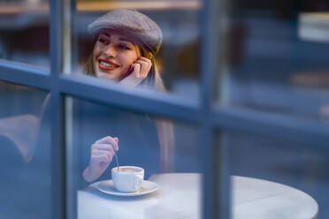 Nachdenkliche Frau mit Kaffeetasse schaut durch das Fenster eines Cafés - GGGF00730