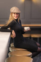 Lächelnde Frau mit Kaffeetasse, die wegschaut, während sie in einem Cafe sitzt - GGGF00733
