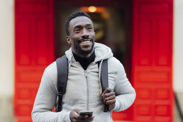 Smiling man with mobile phone looking away while standing outdoors - PGF00343