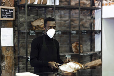 Bäckereibesitzer trägt Schutzmaske bei der Arbeit in der Bäckerei - PGF00353