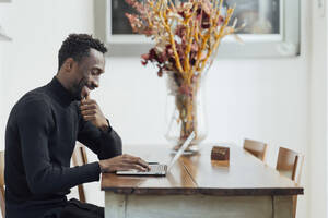 Junger Unternehmer arbeitet am Laptop, während er im Café sitzt - PGF00361