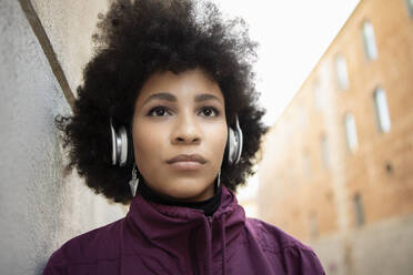 Afro young woman looking away while listening music through headphones - IFRF00260