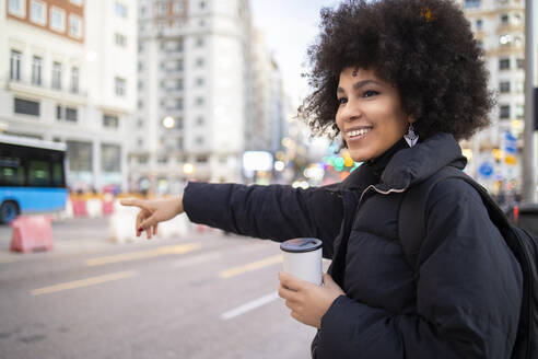 Junge Afro-Frau hält Einweg-Kaffeebecher, während sie auf der Straße ein Taxi ruft - IFRF00278