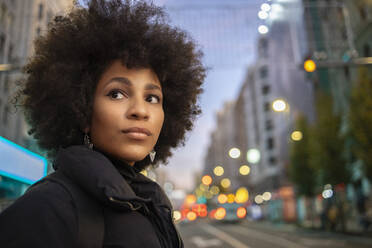 Afro junge Frau im Wegschauen beim Stehen in der Stadt am Abend - IFRF00281