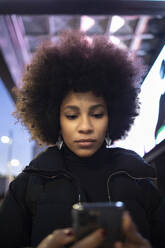 Junge Frau benutzt ihr Smartphone in einer nächtlichen Stadt - IFRF00287