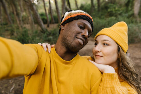 Mann mit Strickmütze, der ein Selfie mit einer Frau macht, während er im Wald steht - EGAF01390