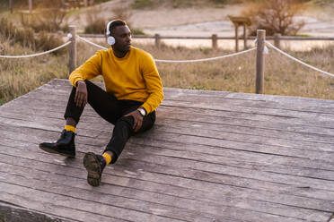 Mann mit Kopfhörern, der wegschaut, während er auf einer Holzbank sitzt - EGAF01406