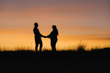 In silhouette of man and woman holding hands while standing against sky - EGAF01407