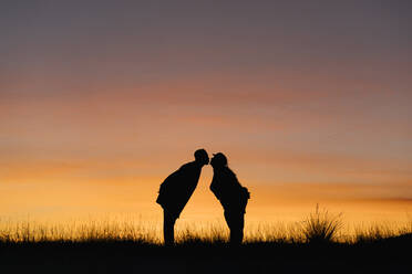 In silhouette of boyfriend and girlfriend kissing while standing against sky - EGAF01408