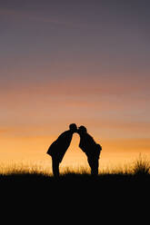 Girlfriend and boyfriend kissing while standing against sky during sunset - EGAF01409
