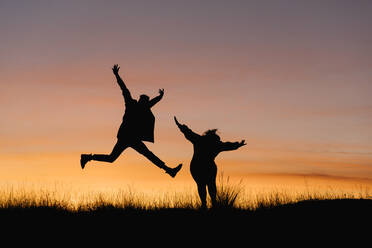 Carefree couple with arms outstretched standing against sky during sunset - EGAF01410
