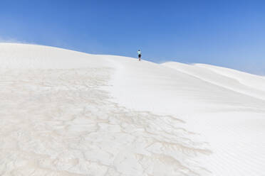 Lone tourist walking across white sand dunes - FOF11855