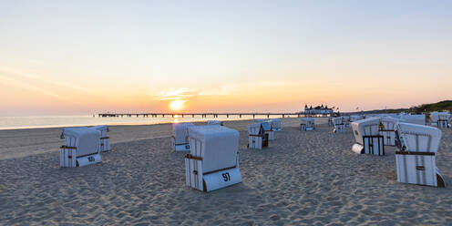 Germany, Mecklenburg-Western Pomerania, Ahlbeck, Hooded beach chairs on sandy coastal beach at sunrise - WDF06452