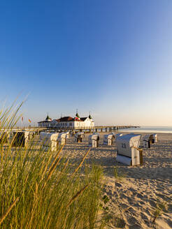 Deutschland, Mecklenburg-Vorpommern, Ahlbeck, Strandkörbe mit Kapuze am sandigen Küstenstrand mit Badehaus im Hintergrund - WDF06454