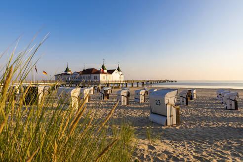 Deutschland, Mecklenburg-Vorpommern, Ahlbeck, Strandkörbe mit Kapuze am sandigen Küstenstrand mit Badehaus im Hintergrund - WDF06455