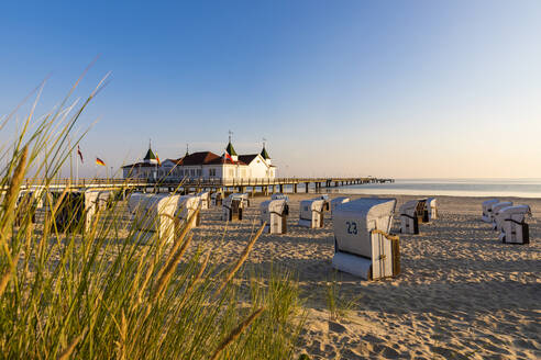 Germany, Mecklenburg-Western Pomerania, Ahlbeck, Hooded beach chairs on sandy coastal beach with bathhouse in background - WDF06455