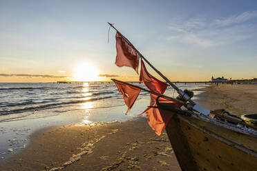 Deutschland, Mecklenburg-Vorpommern, Ahlbeck, Rote Flaggen auf Fischerboot links am sandigen Küstenstrand bei Sonnenaufgang - WDF06461