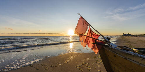 Deutschland, Mecklenburg-Vorpommern, Ahlbeck, Rote Flaggen auf Fischerboot links am sandigen Küstenstrand bei Sonnenaufgang - WDF06462