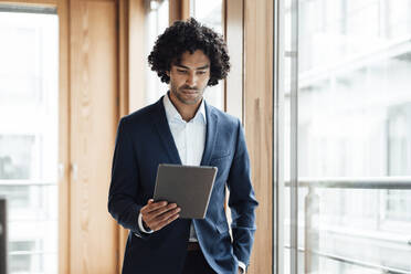 Selbstbewusster junger männlicher Unternehmer mit lockigem schwarzem Haar, der im Büro ein digitales Tablet benutzt - JOSEF02837